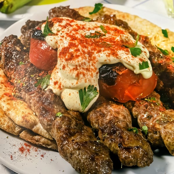 Close-up of Stella’s Greek Cuisine's grilled meat platter with tomatoes, creamy sauce, and paprika.