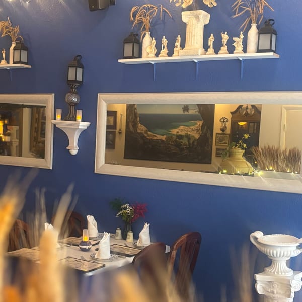 Stella's Greek Cuisine interior with blue walls, Greek decor, mirrors, and set dining tables.
