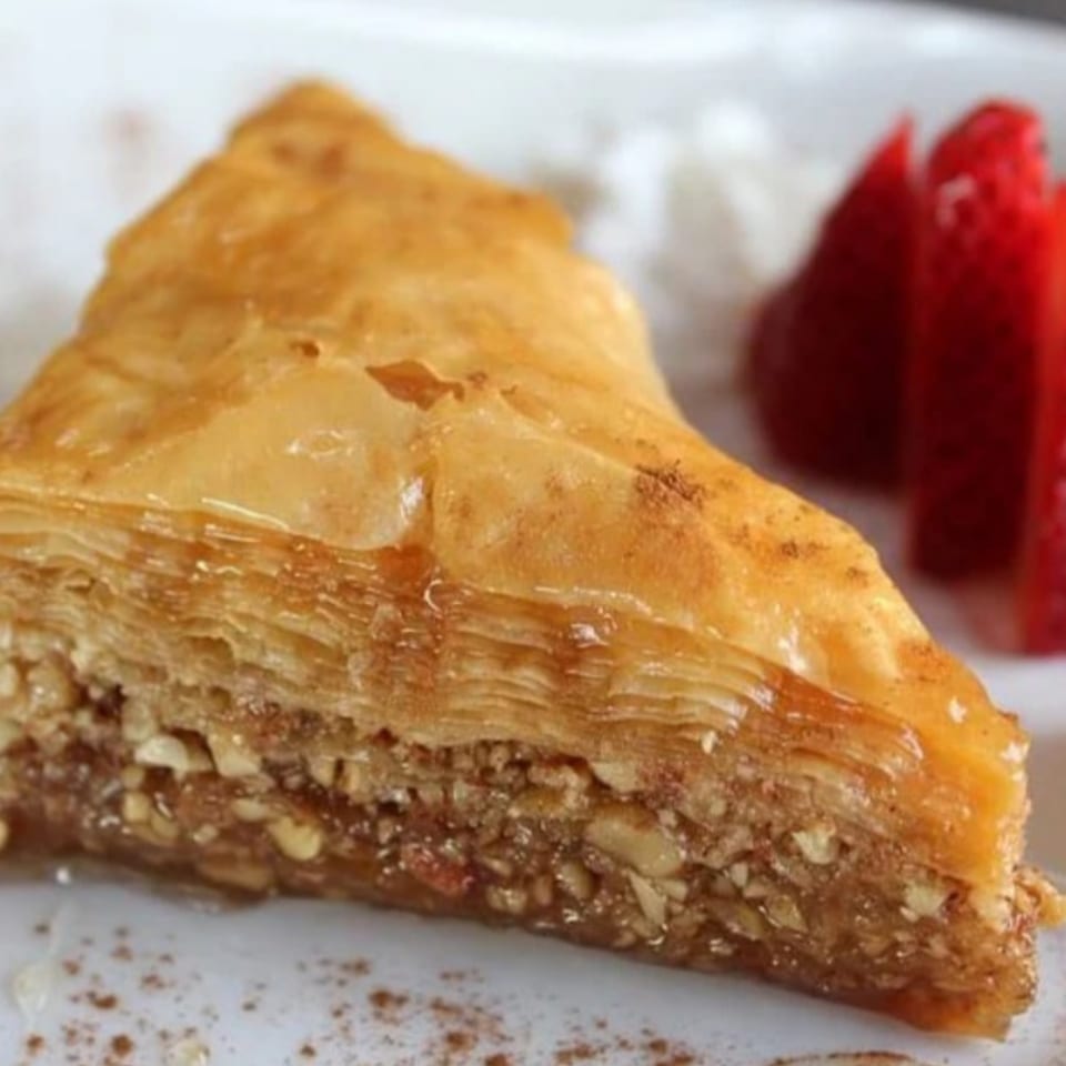 A slice of Stella's Greek baklava with nuts and honey, garnished with strawberries and cinnamon.