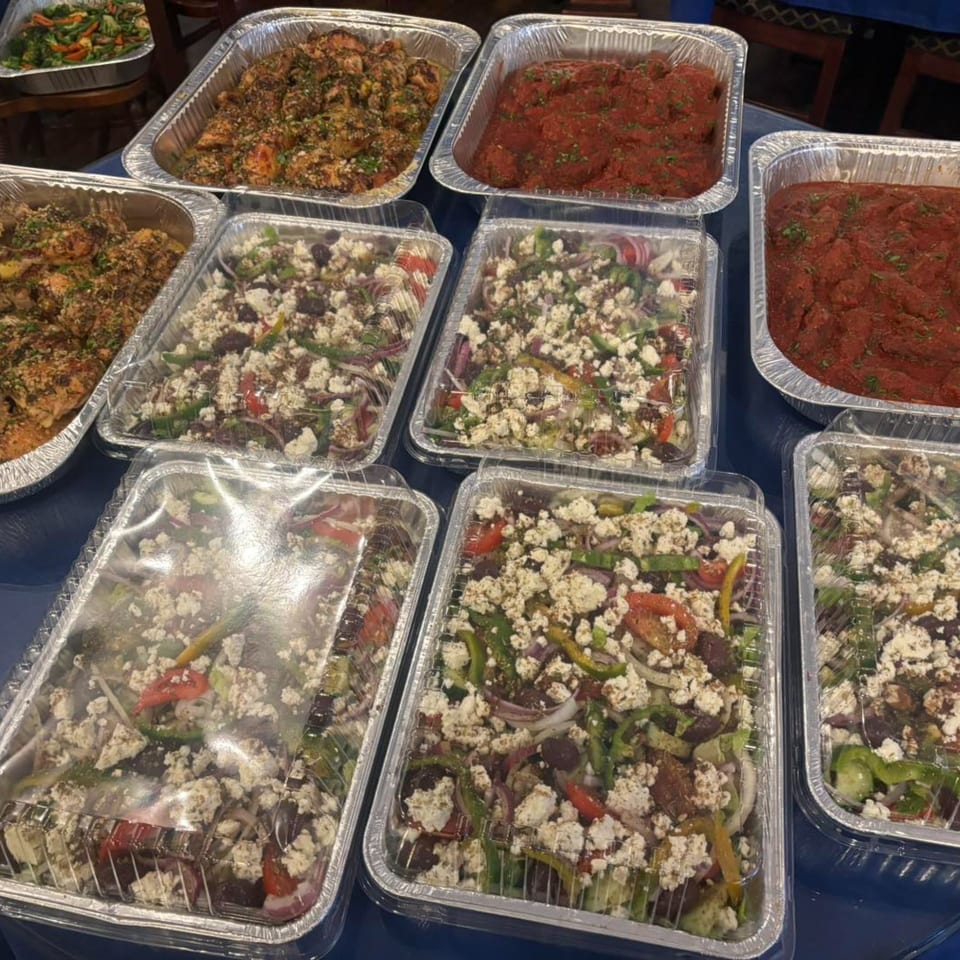 Multiple catering trays of Greek salads, chicken, and red sauce dishes from Stella's Greek Cuisine.