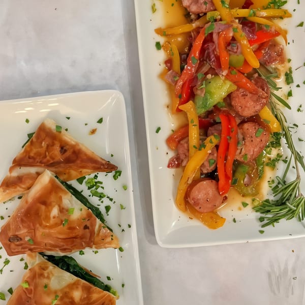 Two plates of Greek appetizers: spanakopita triangles and sausage with colorful bell peppers.