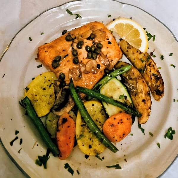 Salmon with capers, lemon, roasted potatoes, and mixed vegetables on a white plate.
