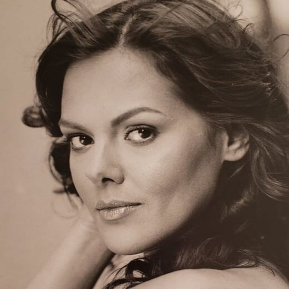 Sepia-toned portrait of a woman with dark, flowing hair looking directly at the viewer.