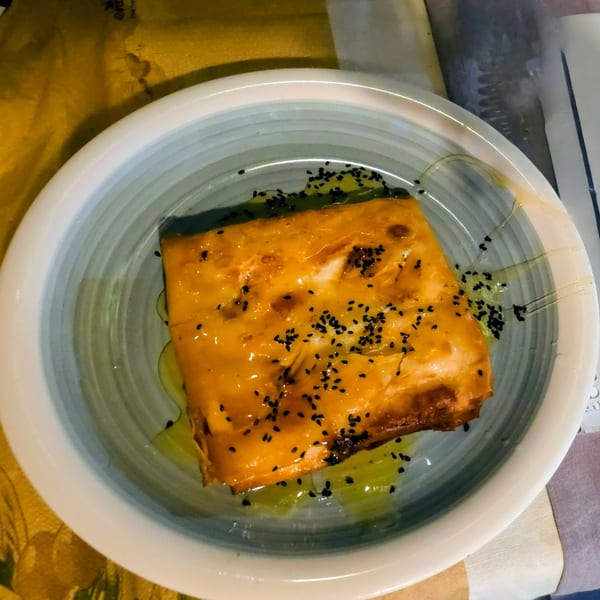 A golden-brown pastry drizzled with honey and sprinkled with black sesame seeds in a blue and white bowl.