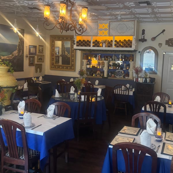 Interior of Stella's Greek Cuisine with blue and white tables, dark wood chairs, and Greek decor.